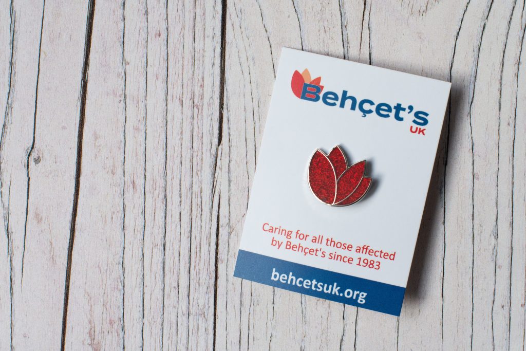 Photo of a sparkly red Behçet's UK tulip badge on a backing card