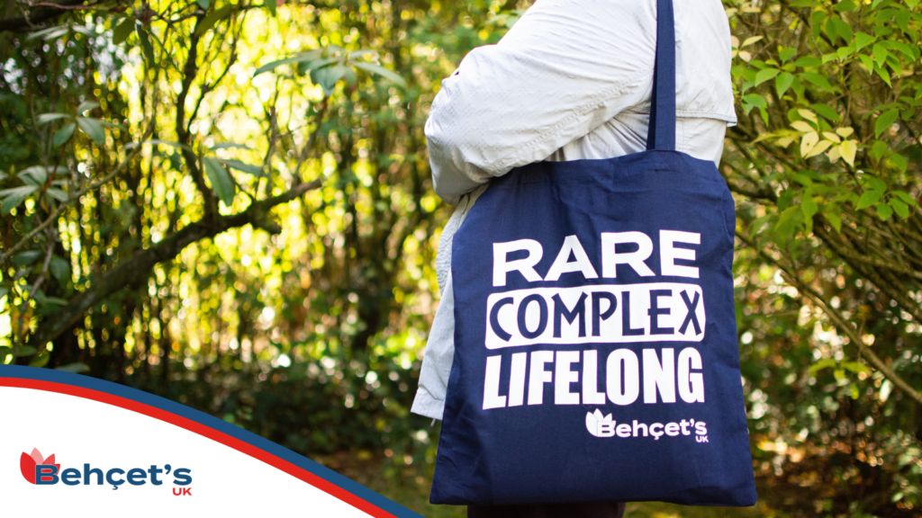Photo of a woman carrying a Behçet's UK tote bag. It is blue with the words 'Rare, Complex, Lifelong' on it.