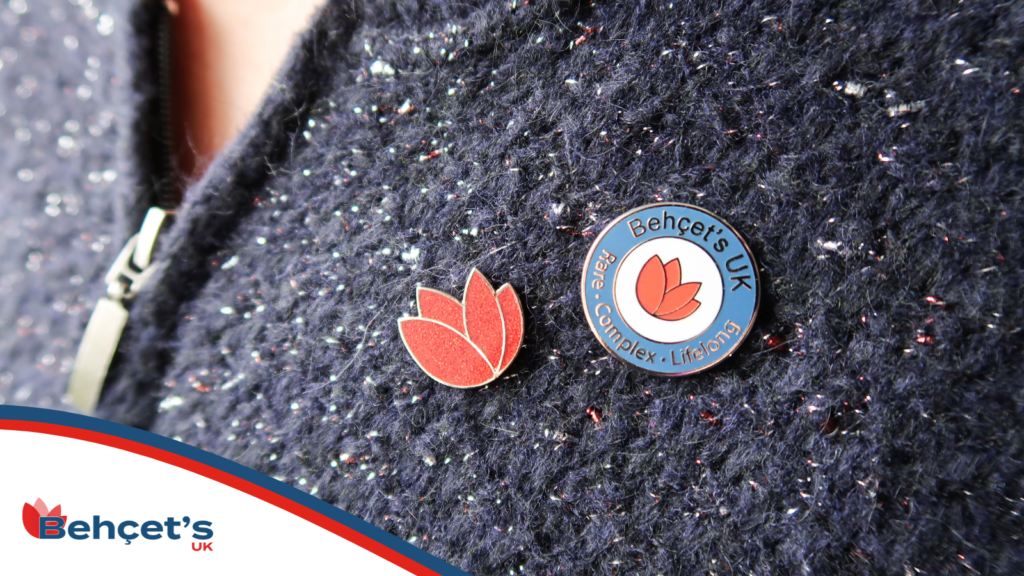 Photo of two Behçet's UK pin badges - a tulip badge, and a logo badge - being worn on a cardigan. 