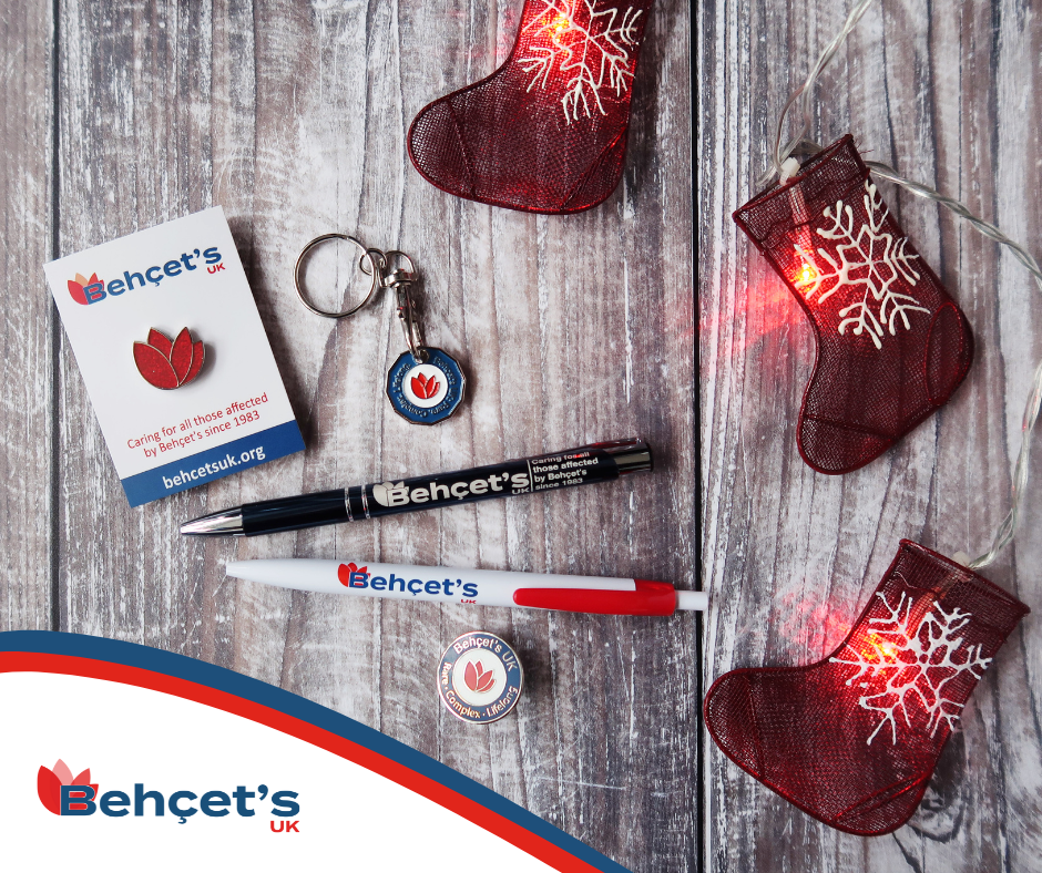 Photograph of a selection of our merchandise on a table - badges, pens, and a keyring, next to some Christmas stocking-shaped fairy lights. 