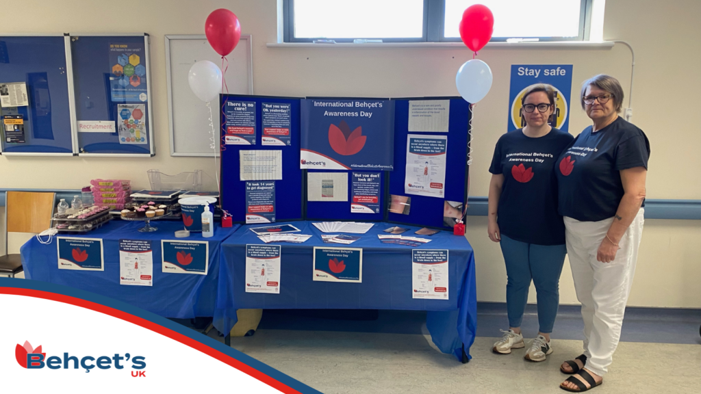 Photo of Behçet's UK supporters Tina and Maxine with their awareness display. A table is covered with posters, leaflets and balloons.
