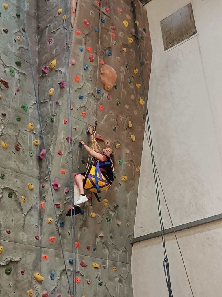 One of our guests who is a wheelchair user climbing the indoor climbing wall using a seated harness