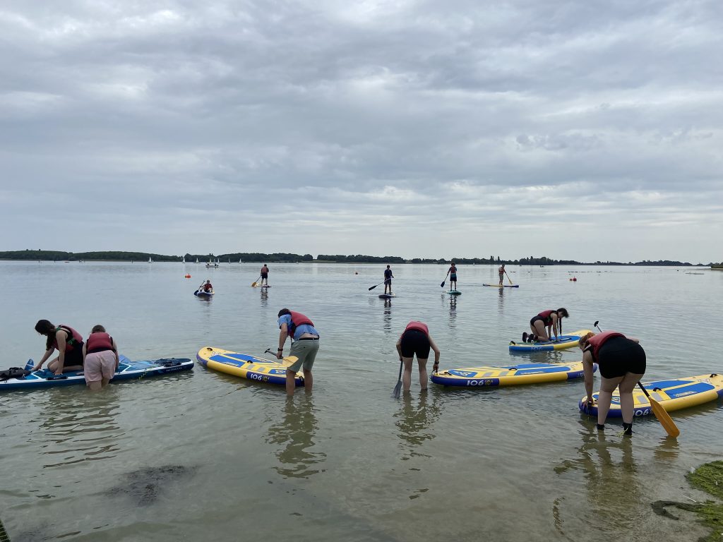 Group of our standup paddle boarders ankle deep in the water getting ready to get on their bords at the start of their session on the water with some of the group already paddling in the background.