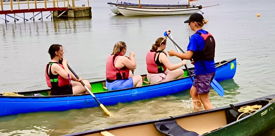 Three of our canoeists in a blue canoe close to shore on the water being given some guidance from an instructor